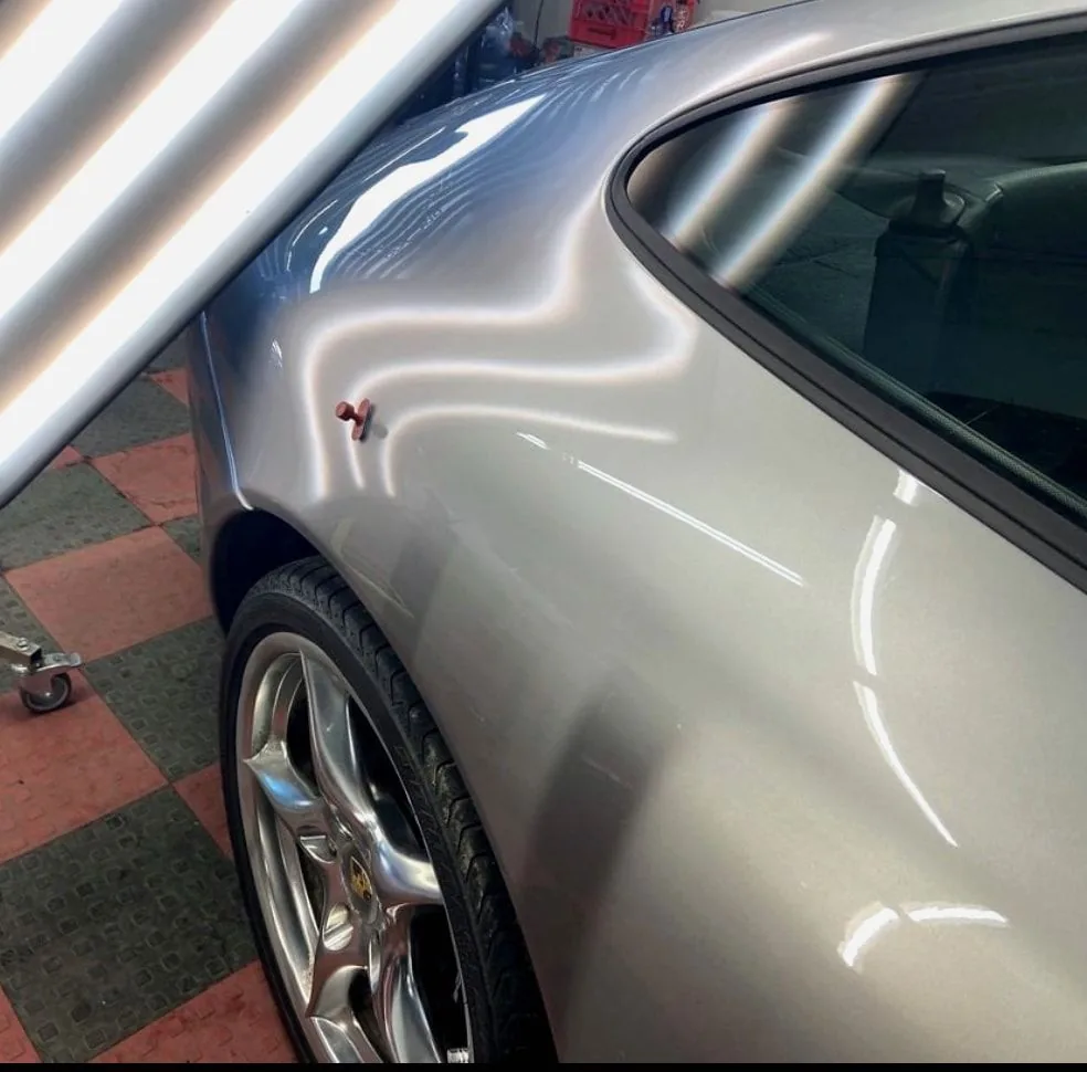 A silver quarter panel under a striped line light, a glue tab on the dent