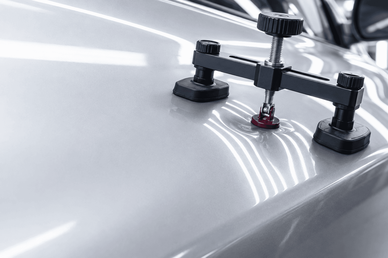 Paintless dent repair bridge puller positioned over a shallow dent on silver paint